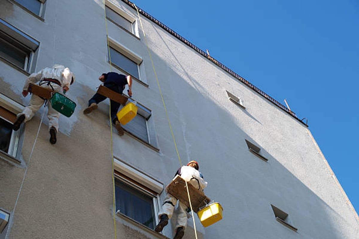 Fasadarbetare på rep renoverar fasaden på ett flerbostadshus